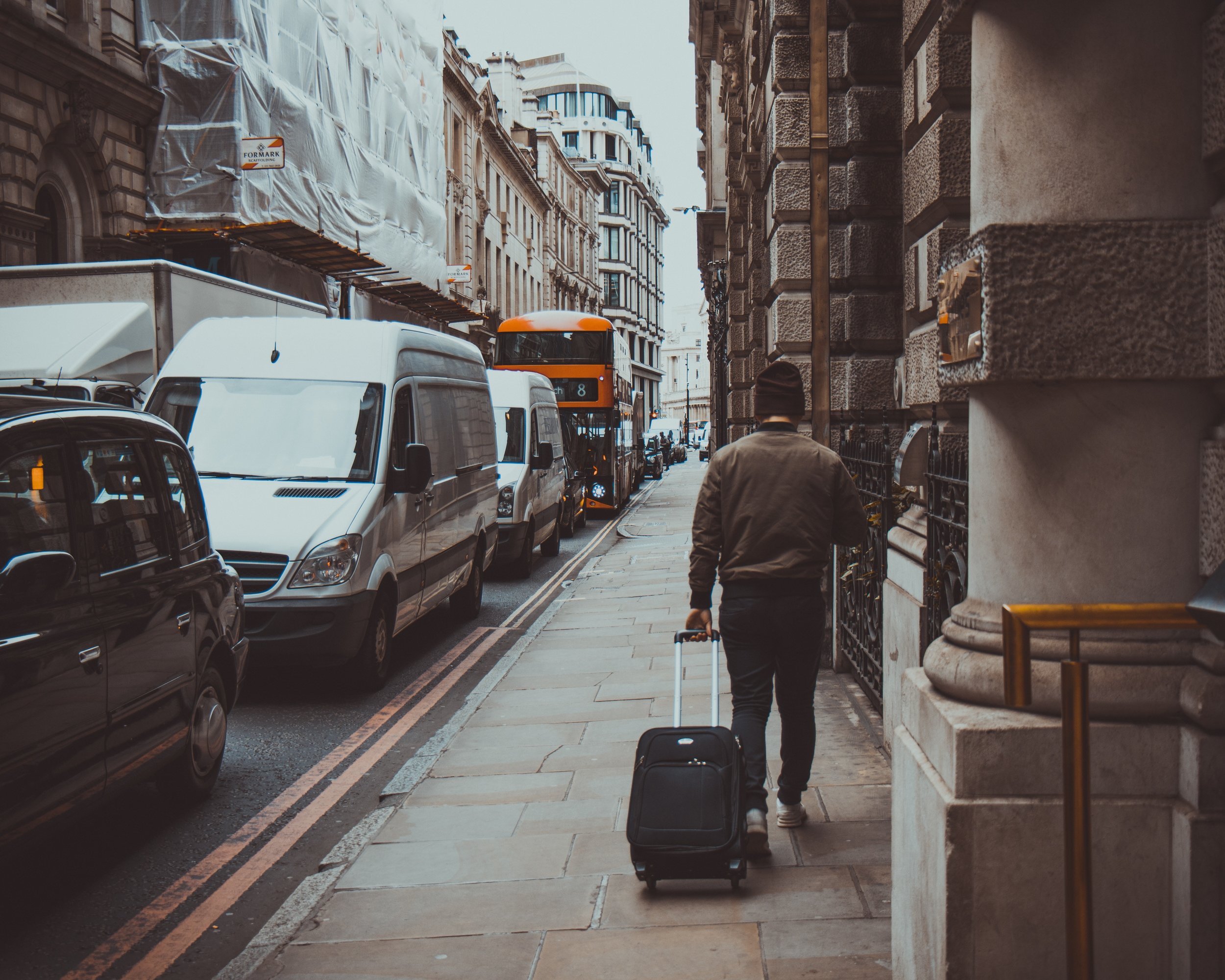 Man walking through the city with suitcase. Photo source Tomáš Gal on Pexels.